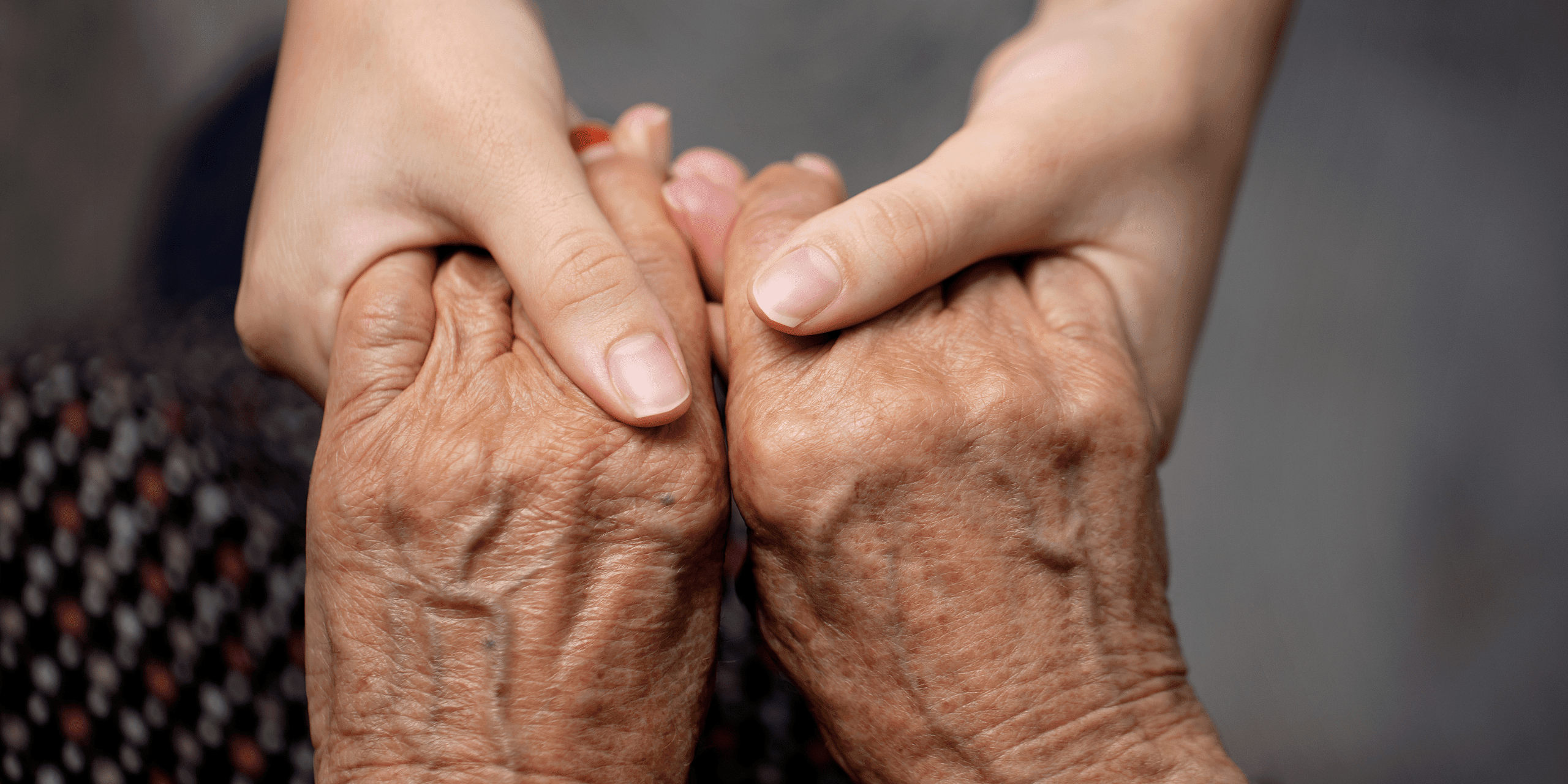 Compassionate caregiver holding an older adult's hands to provide comfort, support, and companionship during in-home care in Lansing, Michigan.